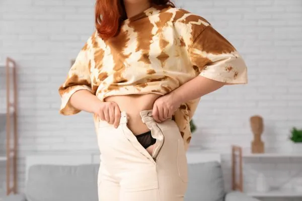 Image of woman trying to do her trousers up after pregnancy weight gain